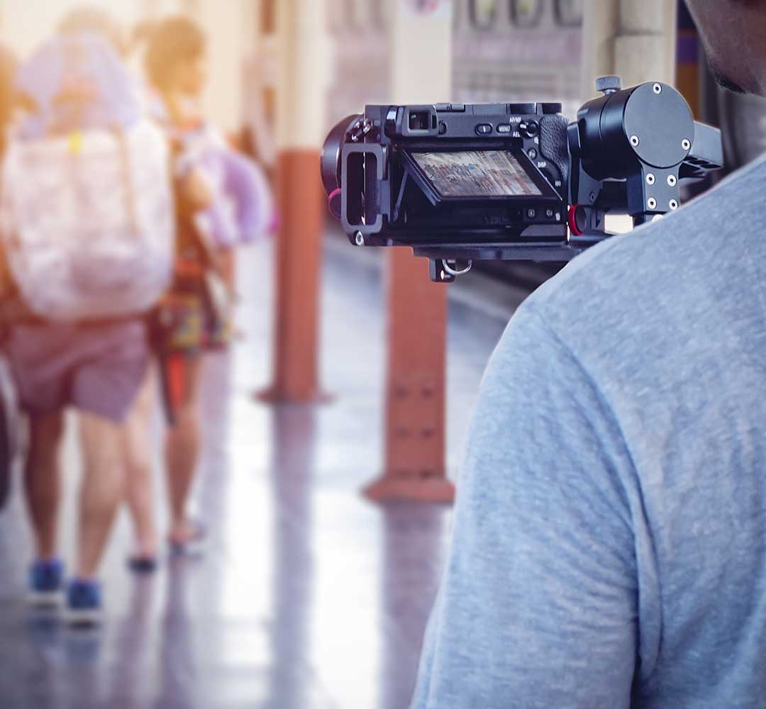 Videographer looking at video camera filming people walking