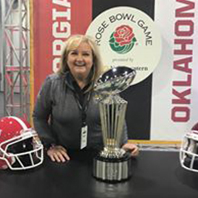 Misty Cato standing in front of black backdrop with football trophy and table in front of her,