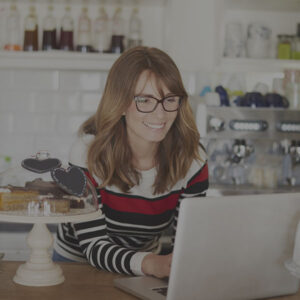 Smiling cafe owner standing at the counter on a laptop