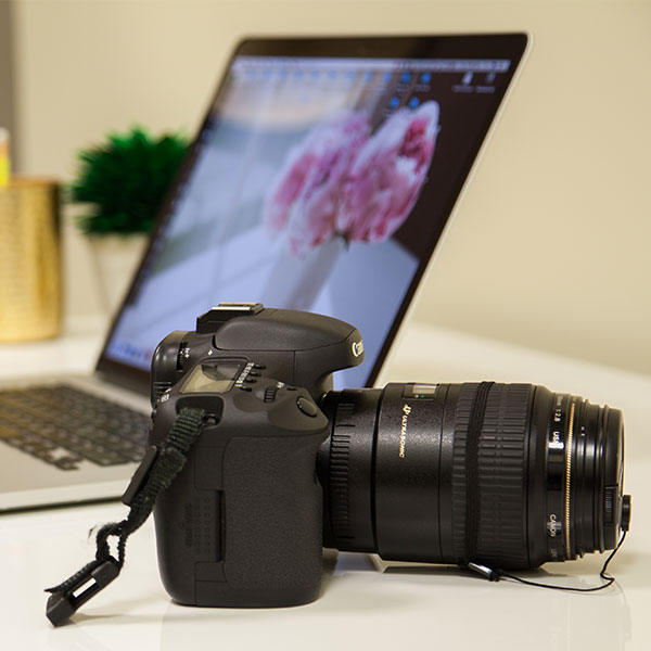 Cannon camera sitting on desk next to laptop.